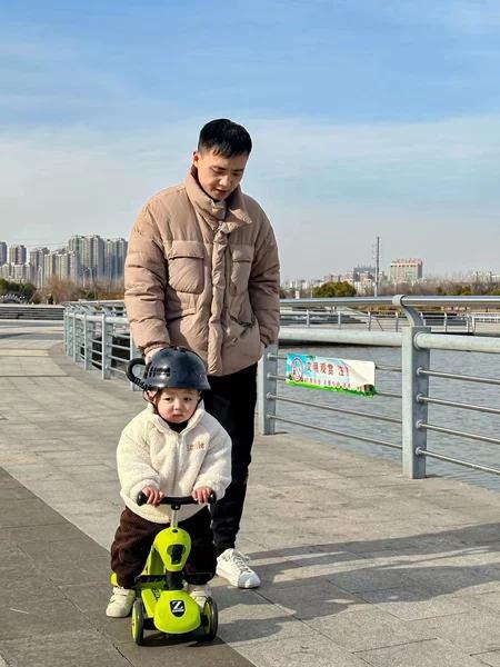 父亲陪娃骑三轮车的城市滨水日常照