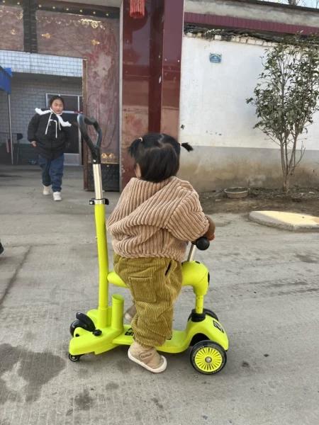 乡村院门口骑亮绿滑板车的可爱孩童背影