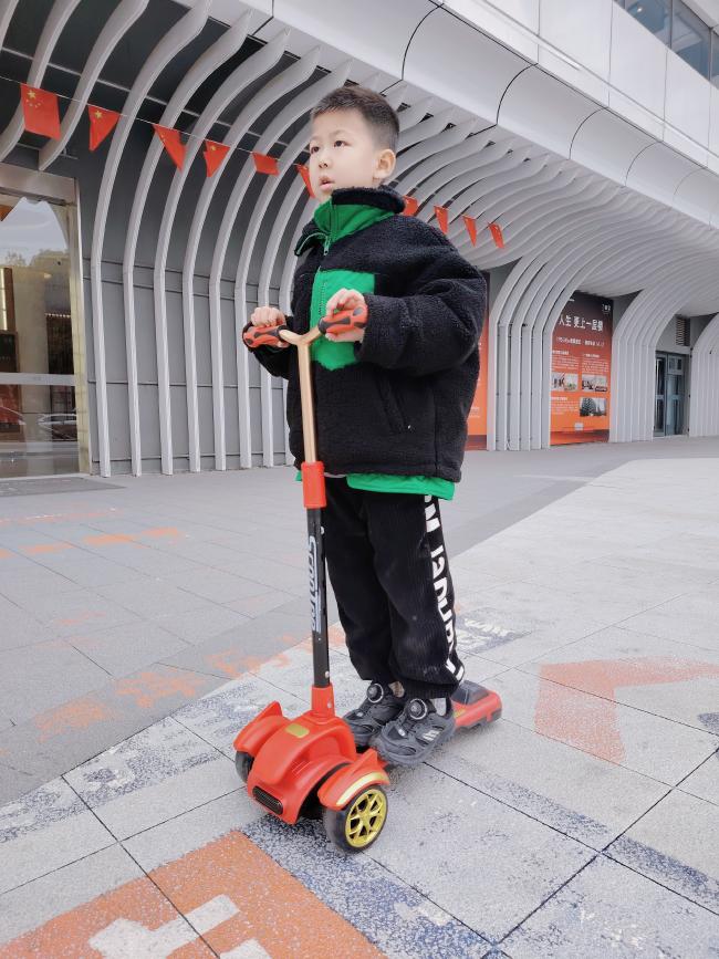 6岁男孩骑红色滑板车，现代建筑前童趣实拍瞬间