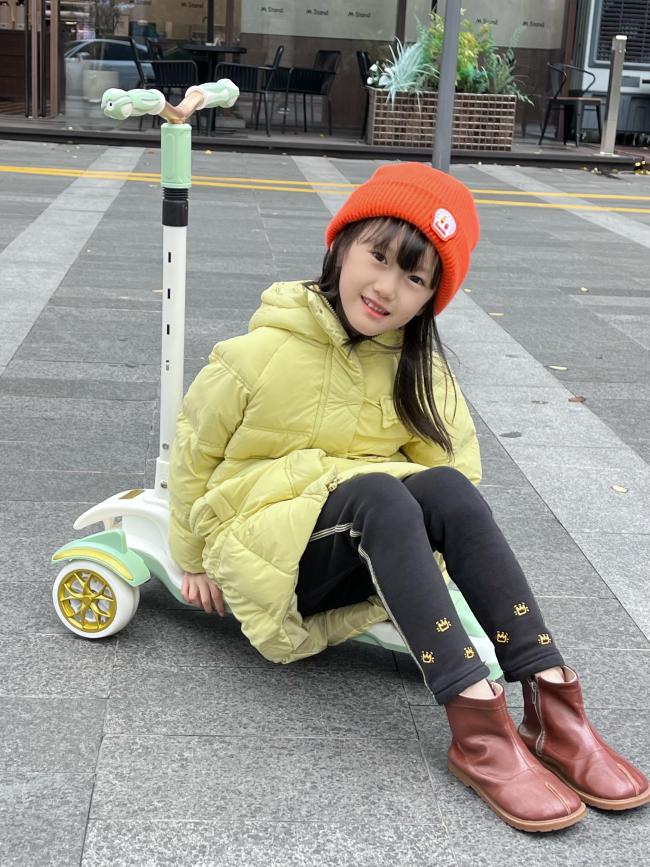 橙色帽子小女孩街拍写真，滑板车上的温暖冬日童趣瞬间
